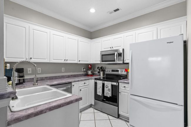 Kitchen with appliances with stainless steel finishes, a sink, white cabinetry, ornamental molding, and light tile patterned floors | Image 16