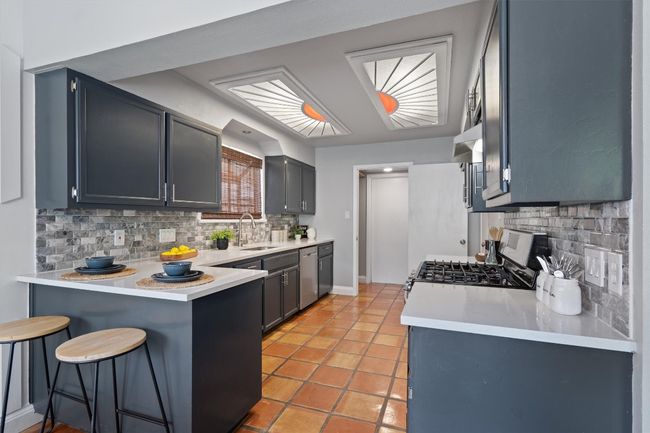 Kitchen featuring appliances with stainless steel finishes, a peninsula, decorative backsplash, a kitchen breakfast bar, and light countertops | Image 10