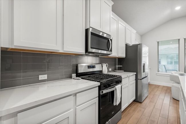 Kitchen featuring stainless steel appliances, lofted ceiling, backsplash, white cabinets, and light wood finished floors | Image 4