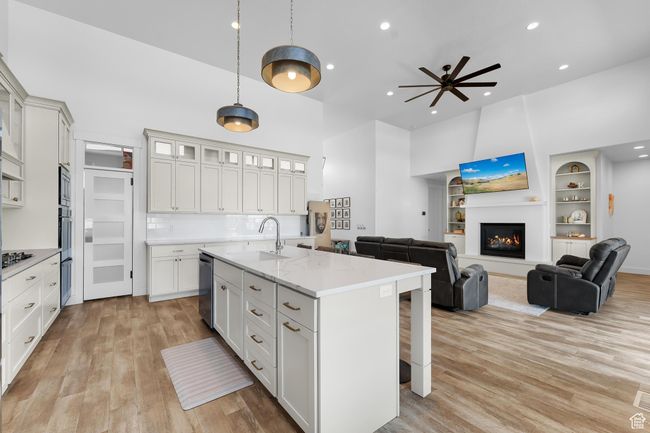 Kitchen featuring a kitchen breakfast bar, light wood-type flooring, a high ceiling, recessed lighting, and a center island with sink | Image 7