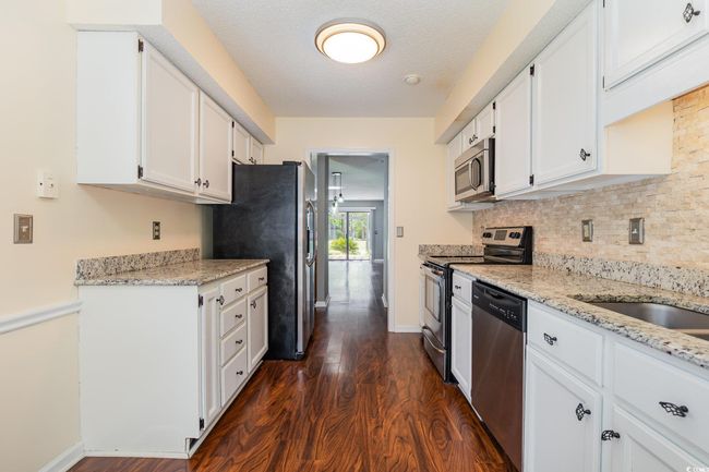 Kitchen featuring decorative backsplash, appliances with stainless steel finishes, white cabinetry, light stone countertops, and dark wood-style floors | Image 11