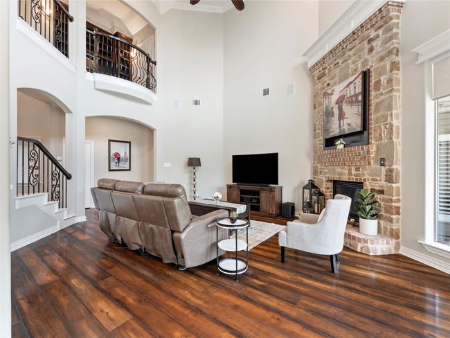 Living room featuring wood-type flooring, stairway, a fireplace with raised hearth, a towering ceiling, and a ceiling fan | Image 16