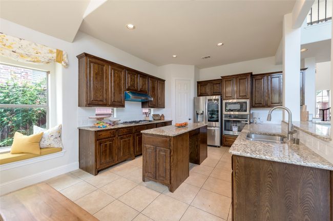 Kitchen with appliances with stainless steel finishes, under cabinet range hood, light stone counters, light tile patterned floors, and a kitchen island | Image 12