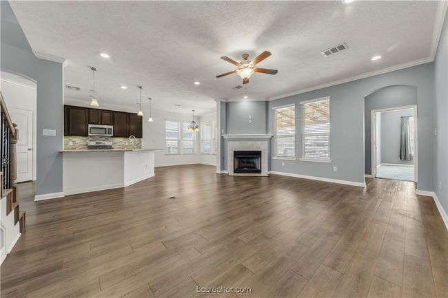 Unfurnished living room featuring dark wood-type flooring, ceiling fan, ornamental molding, and a fireplace | Image 13
