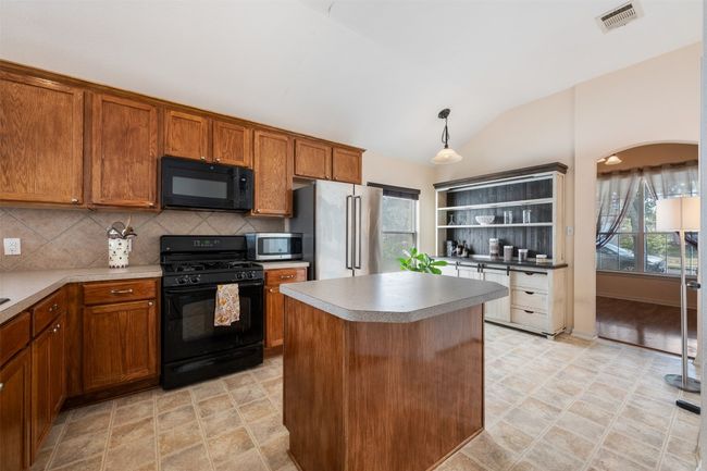 Kitchen featuring visible vents, brown cabinets, black appliances, open shelves, and decorative backsplash | Image 16