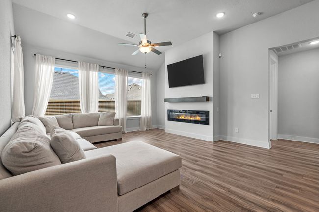 Living area with vaulted ceiling, wood finished floors, a glass covered fireplace, a ceiling fan, and recessed lighting | Image 8