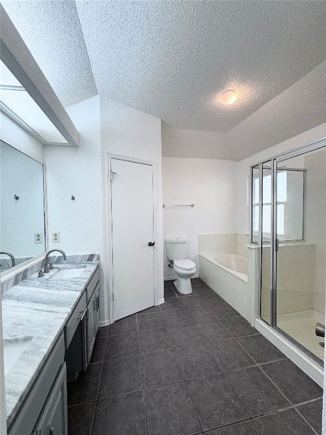 Full bathroom featuring a garden tub, double vanity, a textured ceiling, a shower stall, and dark tile patterned floors | Image 19