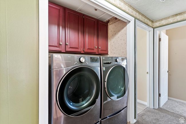 Washroom featuring independent washer and dryer, cabinet space, light carpet, and baseboards | Image 23