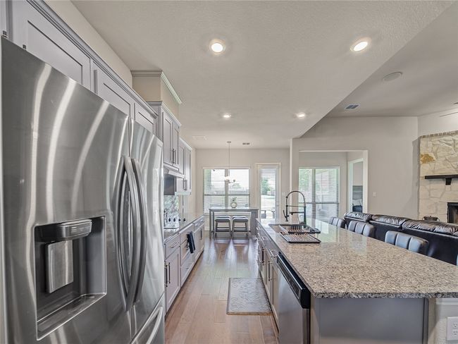 Kitchen featuring stainless steel appliances, a kitchen island with sink, light stone countertops, recessed lighting, and hardwood / wood-style floors | Image 12