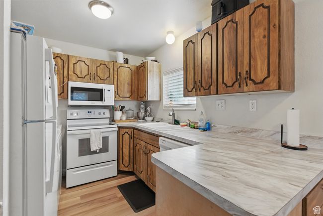 Kitchen with a sink, brown cabinetry, white appliances, light countertops, and a peninsula | Image 7