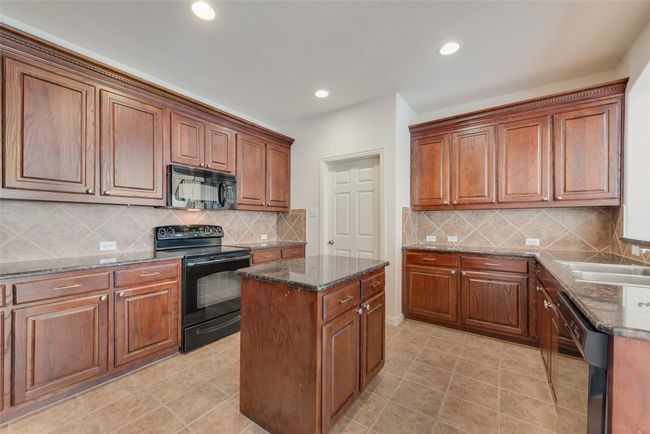 Kitchen with black appliances, dark stone countertops, decorative backsplash, a kitchen island, and recessed lighting | Image 8