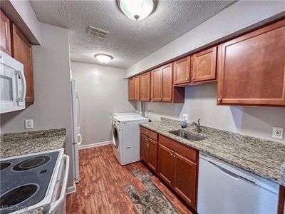 Kitchen with granite countertops, sink, white appliances, laundry area, and a textured ceiling. | Image 3