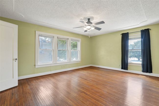 Unfurnished room featuring healthy amount of natural light, hardwood / wood-style flooring, ceiling fan, a textured ceiling, and baseboards | Image 14