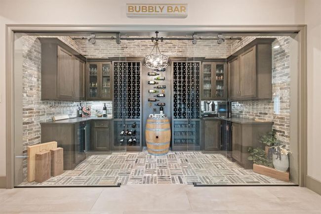 A stylish wine cellar with brick accents and glass doors. It features custom cabinetry, wine racks, a wine fridge, and a barrel centerpiece, creating an elegant space for wine enthusiasts. | Image 11
