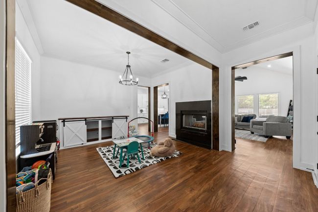 Living area with a chandelier, a multi sided fireplace, crown molding, visible vents, and wood finished floors | Image 17
