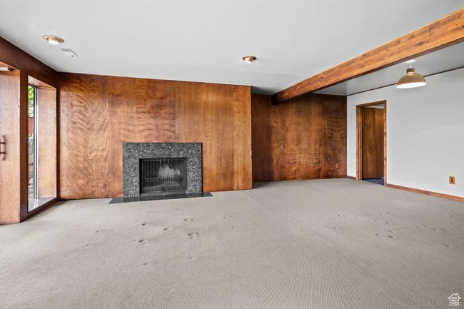 Unfurnished living room with carpet floors, a high end fireplace, beam ceiling, and wood walls | Image 27