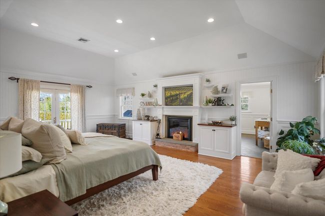 Bedroom featuring high vaulted ceiling, french doors, wood finished floors, a glass covered fireplace, and visible vents | Image 31