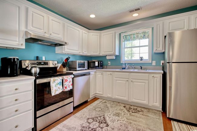 Kitchen with appliances with stainless steel finishes, under cabinet range hood, light countertops, white cabinetry, and a textured ceiling | Image 15