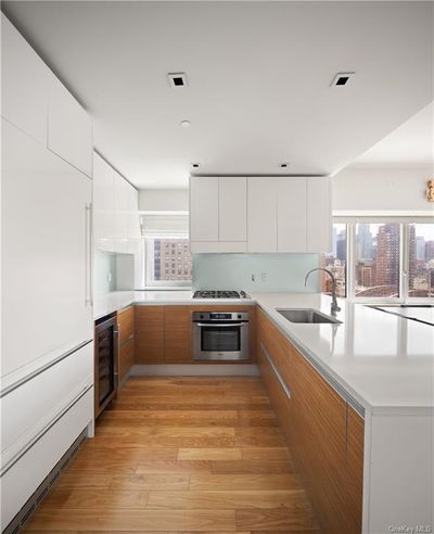 Kitchen featuring white cabinetry, beverage cooler, sink, stainless steel oven, and light hardwood / wood-style floors | Image 3