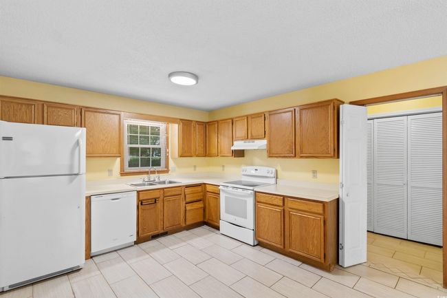 Kitchen with white appliances, under cabinet range hood, light countertops, and brown cabinetry | Image 8