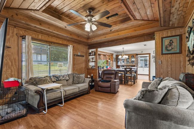 Living room with wooden ceiling, wood walls, a chandelier, light wood-type flooring, and a ceiling fan | Image 4