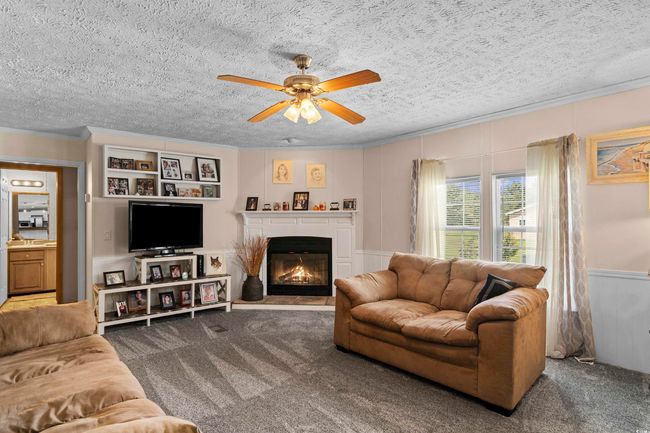 Carpeted living area featuring crown molding, a ceiling fan, a textured ceiling, a glass covered fireplace, and a decorative wall | Image 22