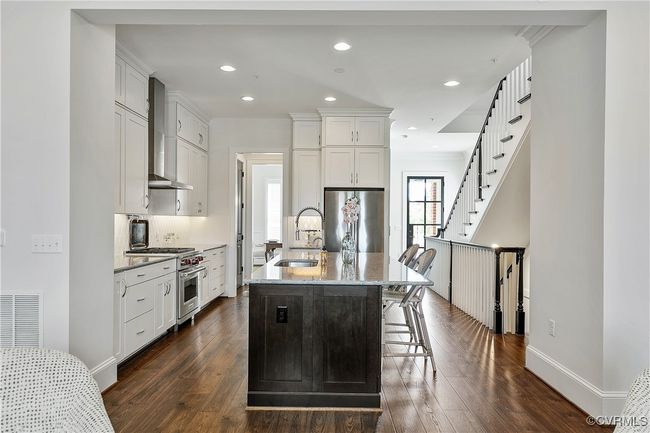 Kitchen featuring a sink, wall chimney range hood, light stone countertops, high end appliances, and a center island with sink | Image 8
