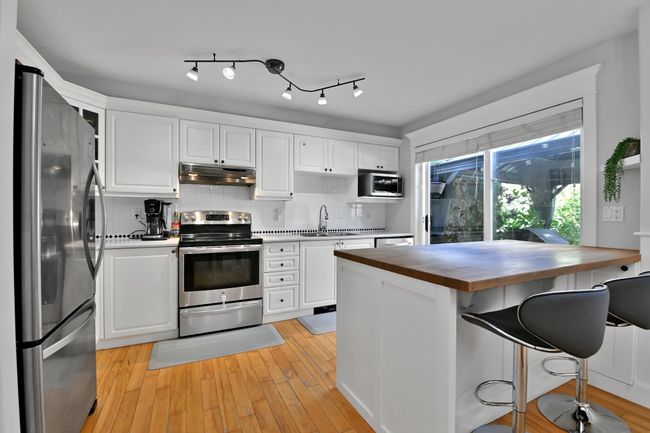 Kitchen with white cabinetry, under cabinet range hood, a sink, stainless steel appliances, and wooden counters | Image 12