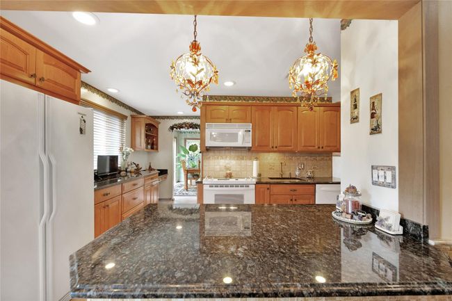 Kitchen with white appliances, a sink, dark stone countertops, and recessed lighting | Image 10