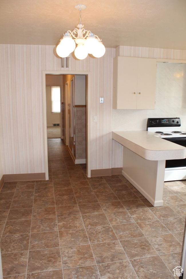 Kitchen with white electric stove, wallpapered walls, a chandelier, light countertops, and a peninsula | Image 5
