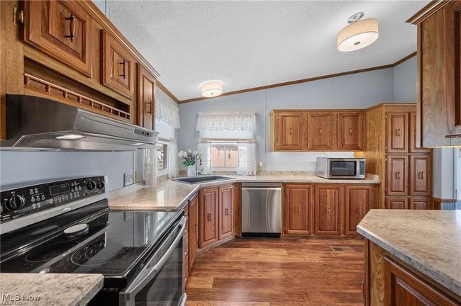 Kitchen with appliances with stainless steel finishes, lofted ceiling, ornamental molding, range hood, and brown cabinets | Image 9