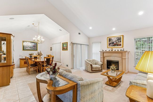 Living area featuring light tile patterned flooring, vaulted ceiling, a chandelier, a fireplace, and recessed lighting | Image 10