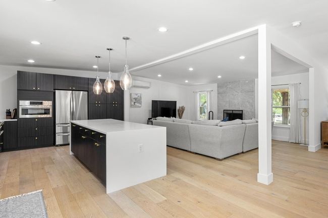 Kitchen featuring light wood-style floors, a center island, appliances with stainless steel finishes, light countertops, and a wall mounted air conditioner | Image 7
