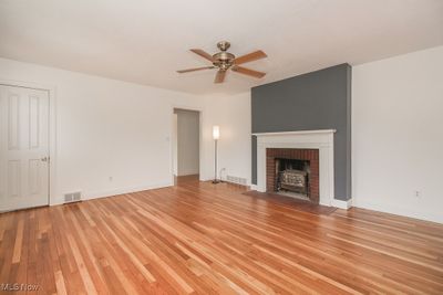 Unfurnished living room featuring ceiling fan, a wood stove, and light hardwood / wood-style flooring | Image 2