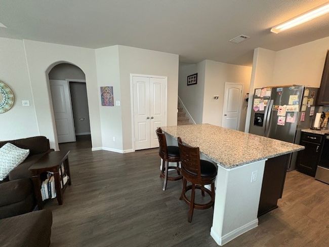 Kitchen featuring fridge, dark wood-style floors, a center island, a breakfast bar, and light stone counters | Image 5