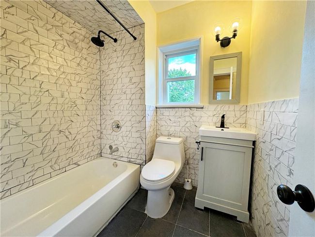 Full bathroom with vanity, tile patterned flooring, tile walls, toilet, and tiled shower / bath combo | Image 7