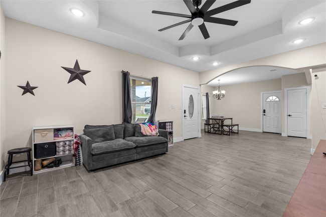 Living area featuring a tray ceiling, recessed lighting, wood finished floors, arched walkways, and a ceiling fan | Image 13