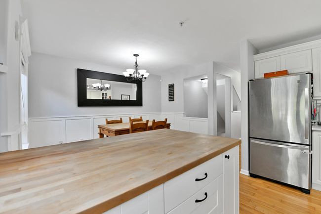 Kitchen with a notable chandelier, freestanding refrigerator, wooden counters, white cabinets, and wainscoting | Image 11