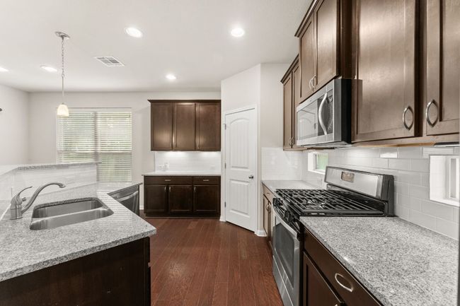 Kitchen with appliances with stainless steel finishes, a sink, dark brown cabinetry, decorative backsplash, and dark wood-style flooring | Image 8
