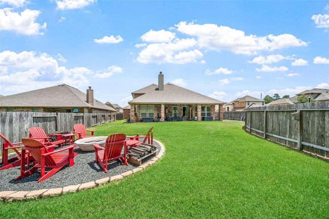 Spacious backyard with a well-maintained lawn, featuring a cozy fire pit area. The yard is enclosed by a wooden fence, and the house has a covered patio area, perfect for outdoor gatherings. | Image 31