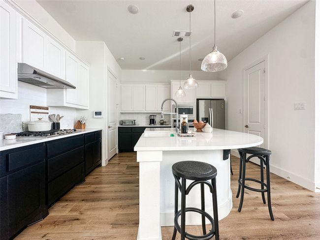 Kitchen featuring appliances with stainless steel finishes, under cabinet range hood, tasteful backsplash, light wood-type flooring, and white cabinets | Image 10