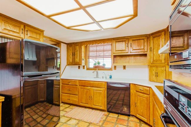 Kitchen with black appliances, light countertops, brown cabinets, and open shelves | Image 4