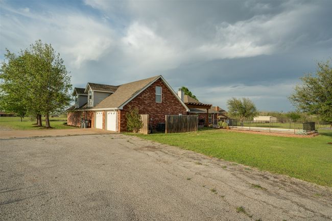 View of side of home with fence, an attached garage, driveway, a lawn, and brick siding | Image 40