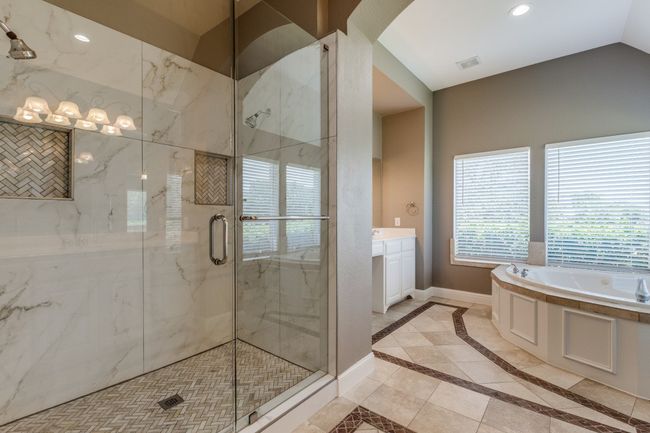 Primary bathroom with plenty of natural light, a bath, a marble finish shower, inlaid floor details, and lofted ceiling | Image 18