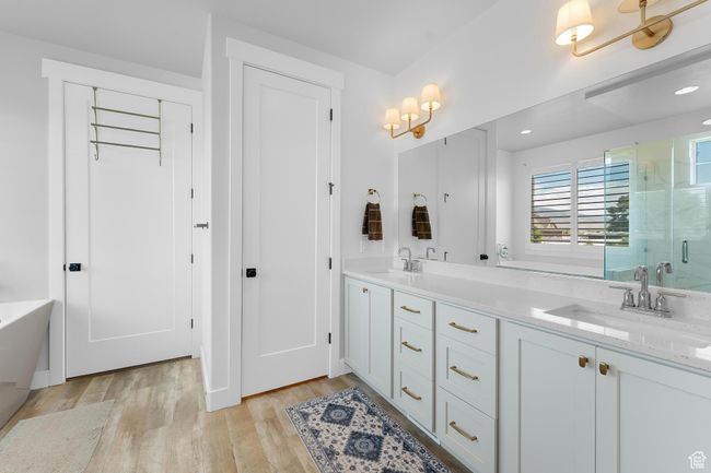 Primary suite bathroom with a shower stall, wood finished floors, double vanity, a soaking tub, and recessed lighting | Image 13