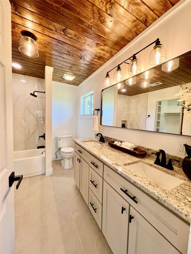 Luxurious primary bedroom ensuite featuring elegant fixtures, a double vanity, and a chic wooden ceiling for a warm, inviting ambiance. | Image 4