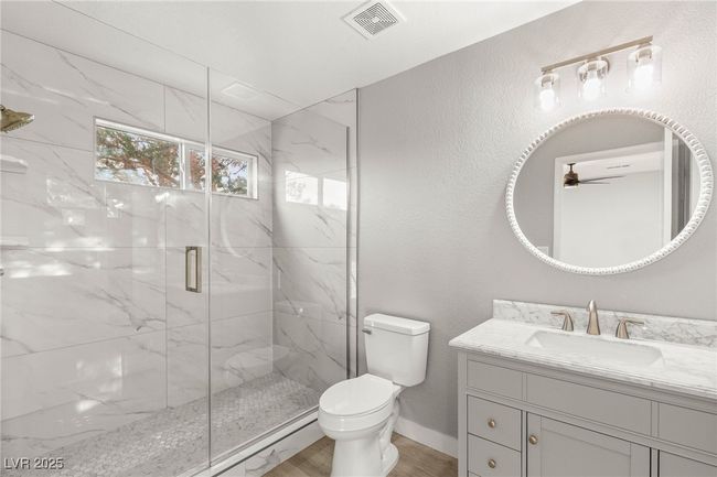 Bathroom featuring visible vents, toilet, vanity, a marble finish shower, and ceiling fan | Image 26