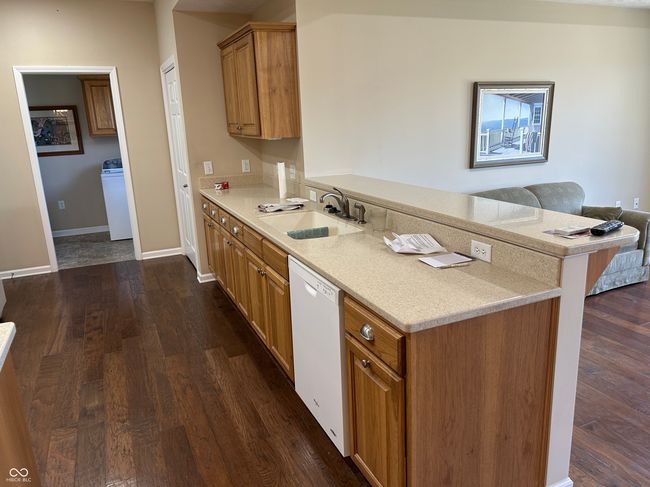 kitchen with light countertops, a sink, white dishwasher, washer / dryer, and a peninsula | Image 6