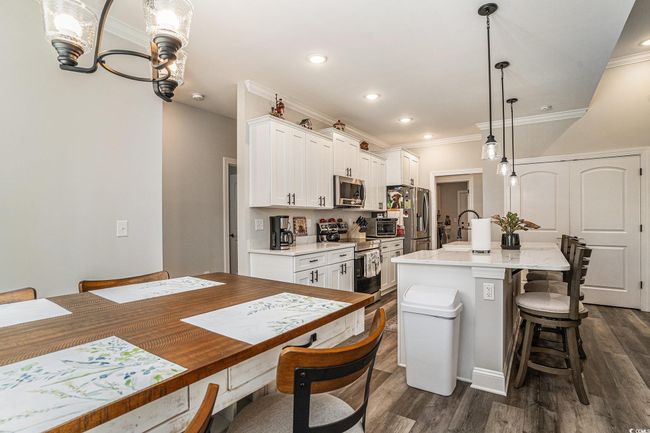 Kitchen featuring stainless steel appliances, a kitchen bar, a kitchen island with sink, ornamental molding, and white cabinetry | Image 12