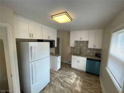 Kitchen with light tile patterned floors, white cabinets, backsplash, stainless steel appliances, and sink | Image 3